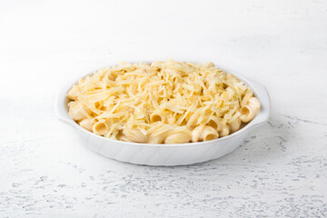 Mac and cheese, American pasta in cheese sauce in a baking dish on a light gray background. Delicious homemade food