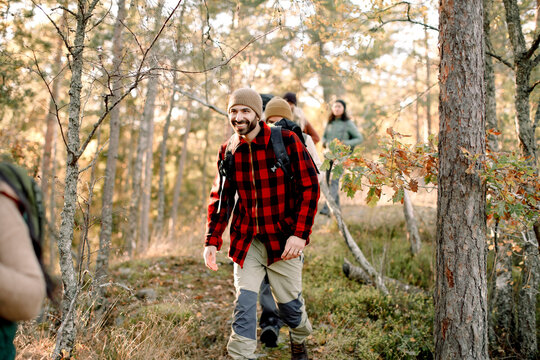 Smiling man hiking with friends amidst trees in forest