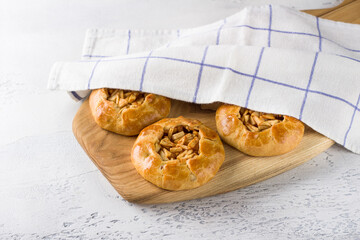 Sweet mini pies with apples and cinnamon on a wooden board with a napkin on a light gray background. Delicious homemade food