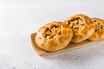 Sweet mini pies with apples and cinnamon on a wooden board with a napkin on a light gray background. Delicious homemade food
