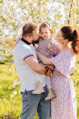 happy family. a mom and a dad with a baby daughter in a blooming spring garden. 