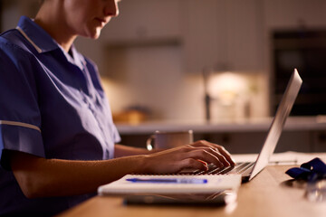 Close Up Of Woman Wearing Medical Scrubs Working Or Studying On Laptop At Home At Night
