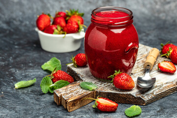 Strawberry jam in the glass jar with fresh berries on dark table