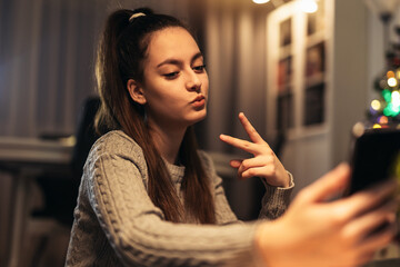 Smiling teenage girl taking selfie at home using smartphone