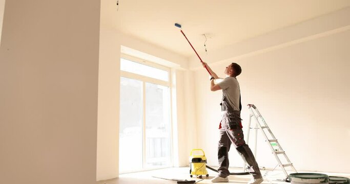 Builder manually paints the ceiling inside house and building