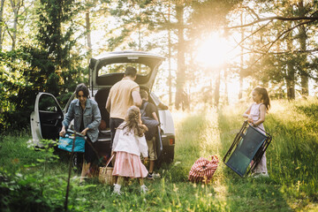 Family helping each other while unloading stuffs from car trunk in forest