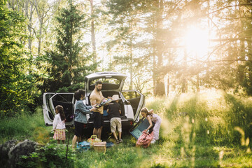 Family unloading stuffs from car trunk in forest on sunny day