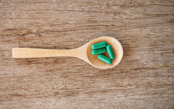 Top view of green herb capsule in wooden spoon on wood desk. Herbal medicine concept. 