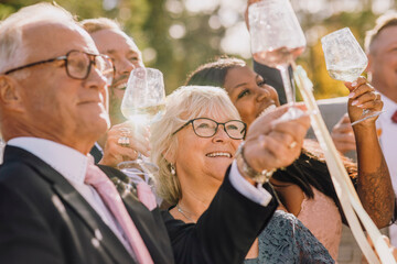 Smiling friends and family toasting wineglasses celebrating during wedding on sunny day