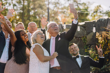 Happy newlywed senior couple taking selfie with family and friends through smart phone