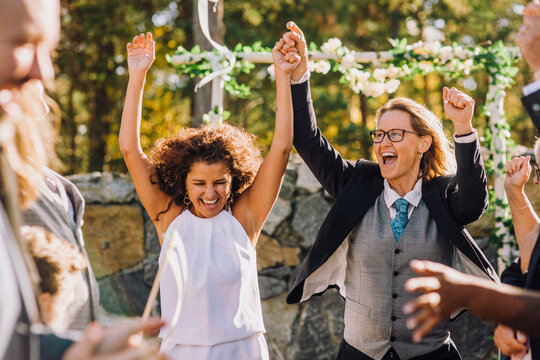 Happy lesbian couple holding hands dancing amidst family and friends during wedding celebration