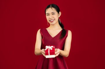 Young beautiful asian woman in red luxury dress holding and giving present red box white bow pose looking and smiling red background.