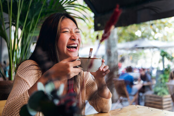 young asian woman laughing while drinking coffee during her date at a coffee shop, concept of relaxation and leisure