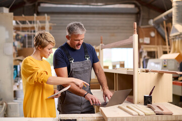 Obraz na płótnie Canvas Female Apprentice Learning Skills From Mature Male Carpenter In Furniture Workshop