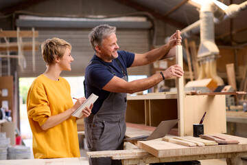 Female Apprentice Learning Skills From Mature Male Carpenter In Furniture Workshop