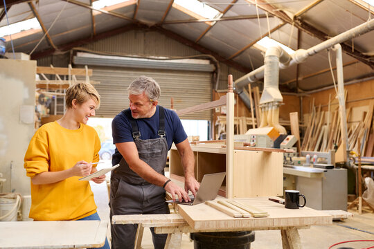 Female Apprentice Learning Skills From Mature Male Carpenter In Furniture Workshop