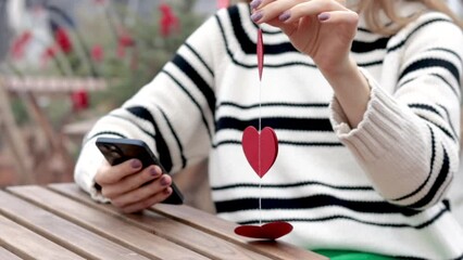 woman sitting in on table with paper hearts garland in one hand using smartphone with another,girl hugging red balloon heart shape.celebrate love valentine day coffee shop inside transparent balloon