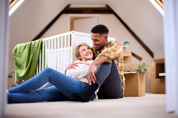 Couple Expecting Baby Relaxing In Nursery Of New Home Together With Moving In Boxes
