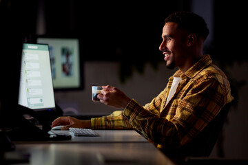 Businessman Working Late In Office With Face Illuminated By Computer Screen Drinking Coffee
