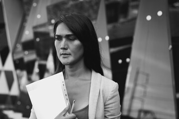 Asian business woman portrait with concerned look holding files folder outside office building....