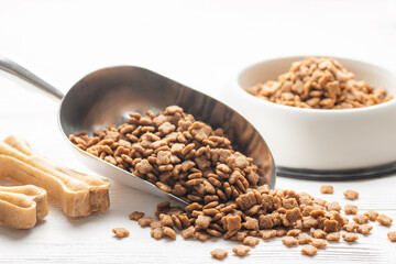 Dry pet food in scoop on white wooden background.
