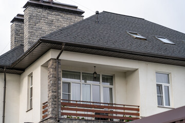 Stucco house with balcony and drainage system on metal roof. Сhimney pipes is finished externally...