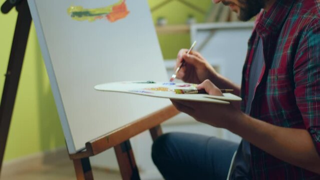 A painter handsome man is painting very carefully something beautiful on a big canvas in his art room