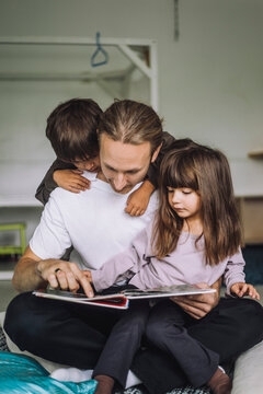 Male teacher reading story for children at day care center