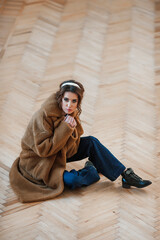 sexy girl dressed in a fur coat posing indoors sitting on the floor; warm long fur coat