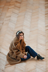 sexy girl dressed in a fur coat posing indoors sitting on the floor; warm long fur coat