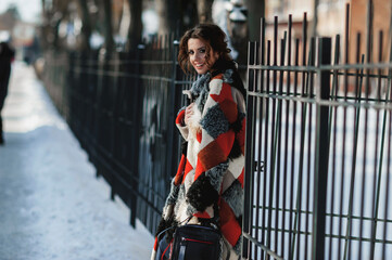 a sexy girl dressed in a long fur coat poses on the street; walks along the winter street holding a handbag