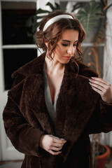 sexy girl dressed in a fur coat and posing indoors on the background of the door; warm long fur coat