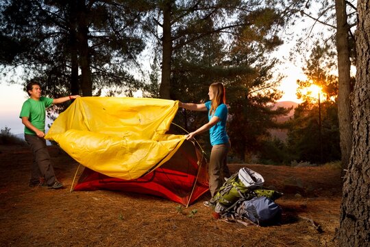 Ethnic couple putting a rainfly on a tent while backpacking in the mountains.