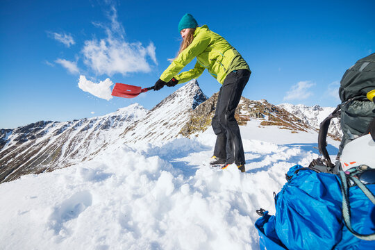 Female Hiker Shoveling Snow To Make Space For Tent, Moskenesoya, Lofoten, Norway