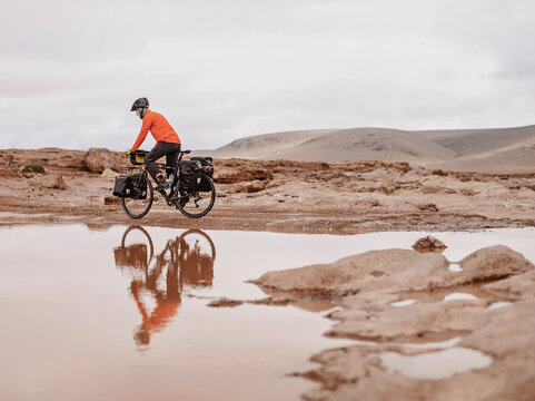 A bike packer is reflected in water on a cold day, Taliouine, Morocco