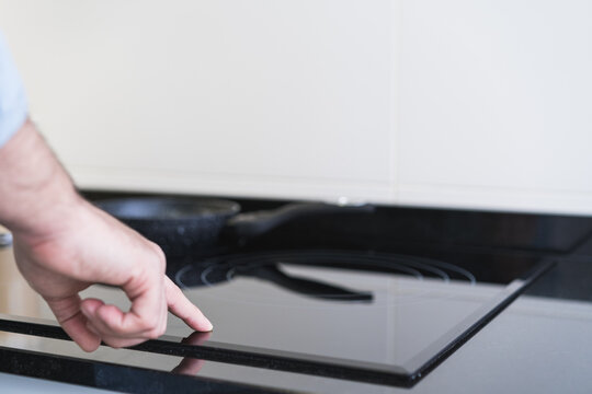 Man cooking in the kitchen in a denim shirt. An anonymous is pressing the button on the ceramic hob