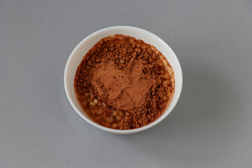 Cooked wheat in a bowl with cocoa on top photographed on a gray background.