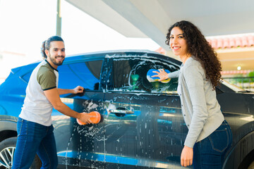 Cheerful couple using a sponge to wash the car