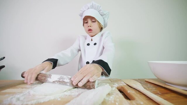 Close view of little chef's hands who is focused on rolling out pastry with a rolling pin preparing it for baking homemade pizza or bread in oven. A boy helps in the kitchen