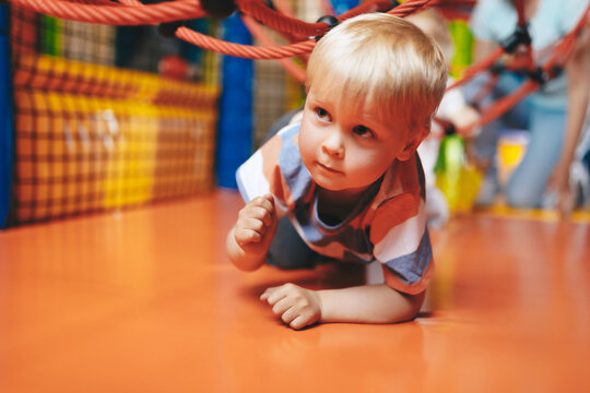 Little boy crawling at amusement park. Happy kid playing at kindergarten. Happy boy playing in indoor playground on net trail - Powered by Adobe