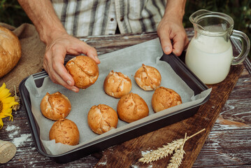 freshly baked pies in the hands of a male baker, buns on a baking sheet with milk on a brown wooden...