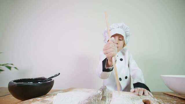 Portrait of a little baker focused on pricking the pastry with a wooden paddle preparing the daugh for baking a homemade pizza or bread. A 5 years old caucasian boy helps in the kitchen