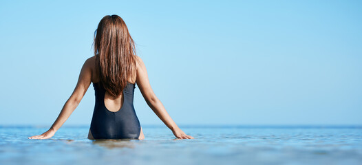 Back, young woman swimming at the beach on vacation in Mauritius and horizon of blue ocean water in...