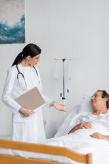 brunette doctor with paper folder talking to elderly patient in clinic.