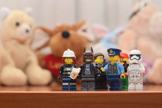 Lego minifigures of Star Wars warrior, batman, firefighter, policeman in front of soft toys in child room. Editorial illustrative image of popular brand constructor. 