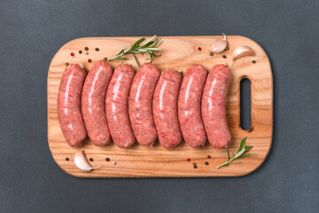 Raw sausages or bratwurst with seasonings on wooden cutting board over black stone table...