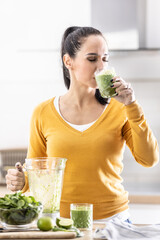 A young woman enjoys a spinach smoothie she made herself. She drinks a vegetable energy drink