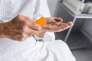 Cropped view of elderly patient holding pills in hospital ward.