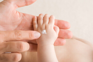 Young adult mother finger applying white moisturizing cream on newborn hand. Care about baby clean...