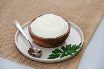 White fermented milk yogurt in a decorative plate, next to a metal spoon, on a brown background